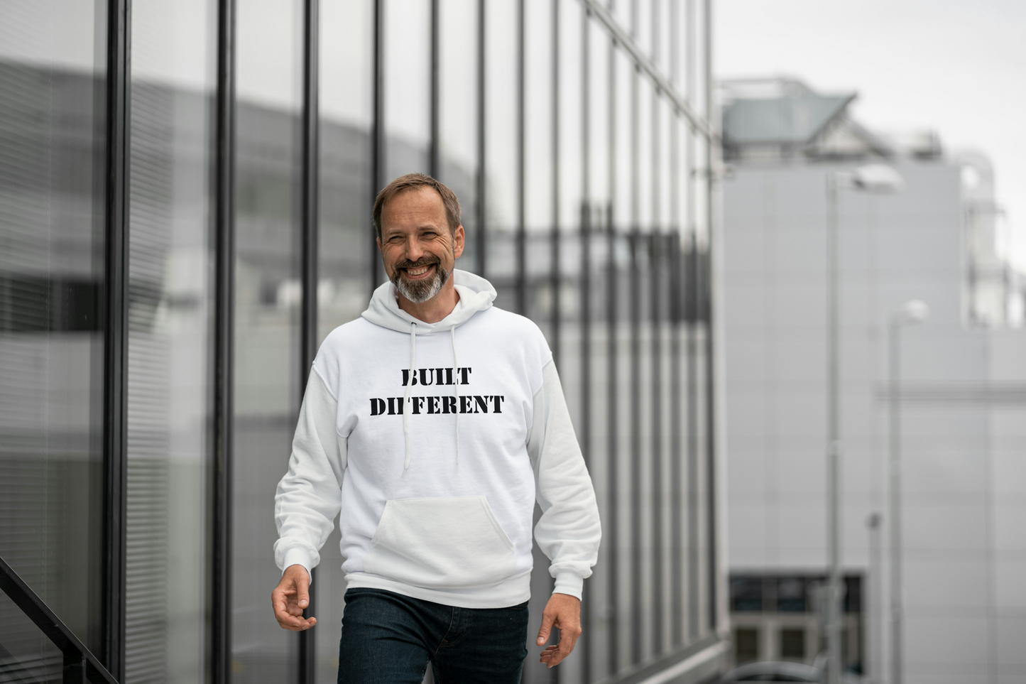 Man wearing a off white hoodie with text, standing in front of a modern building.