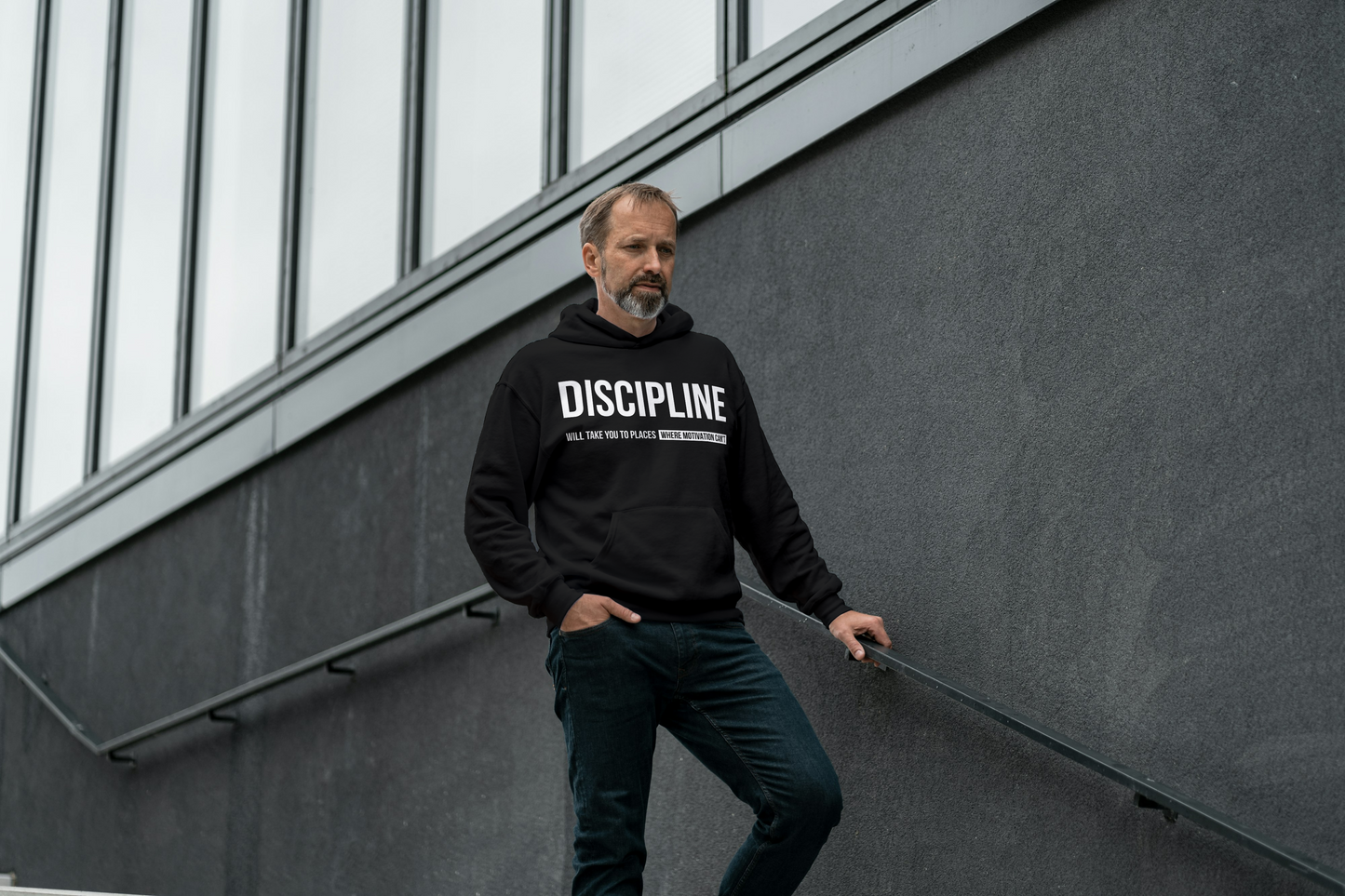 Man wearing a black hoodie with 'DISCIPLINE' text, standing against a modern building.