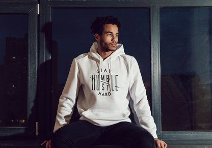 Man wearing a off white hoodie with text, sitting by a window at night.