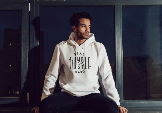 Man wearing a off white hoodie with text, sitting by a window at night.