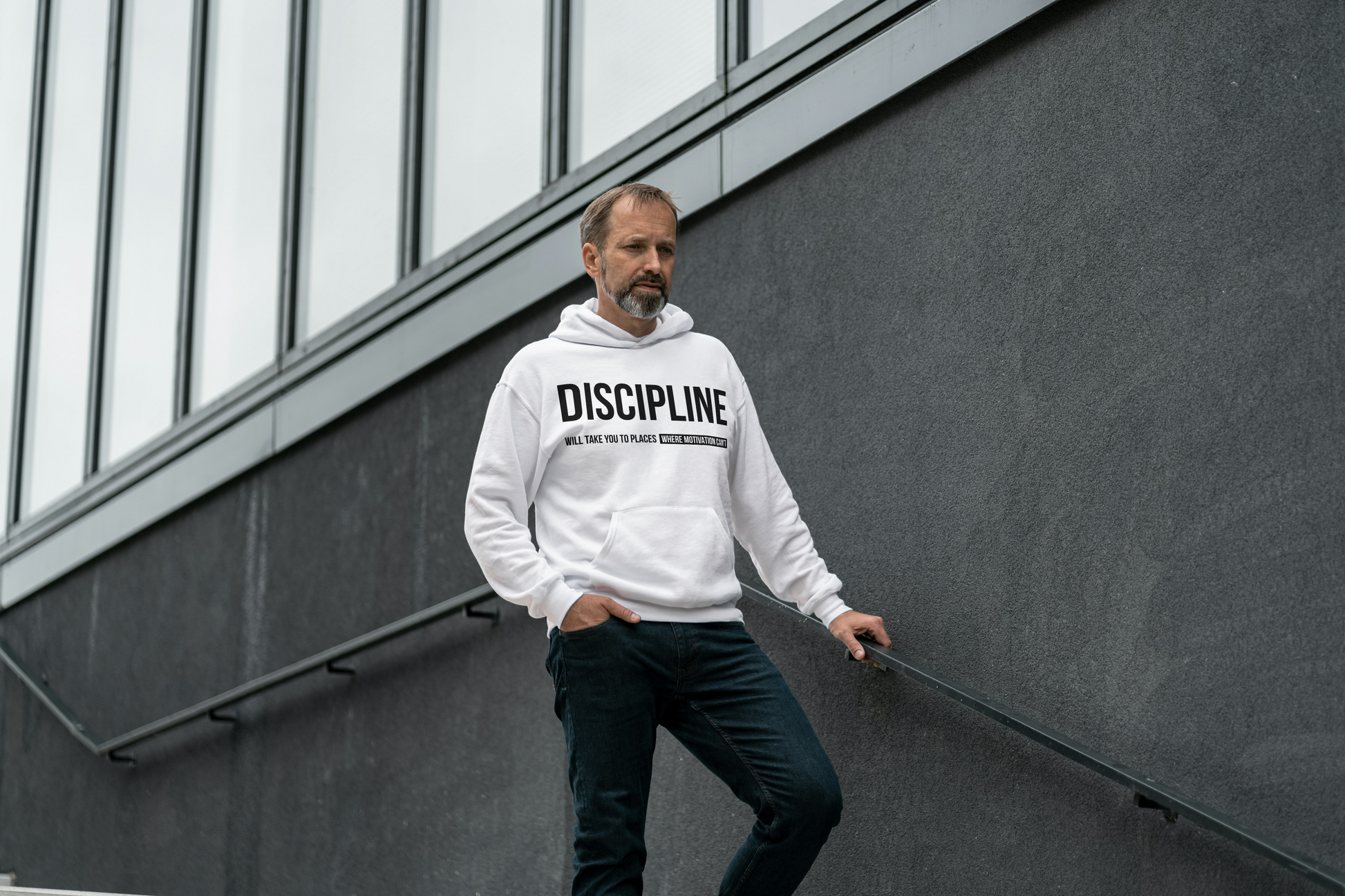 Man wearing a off white hoodie with 'DISCIPLINE' text, standing against a modern building.